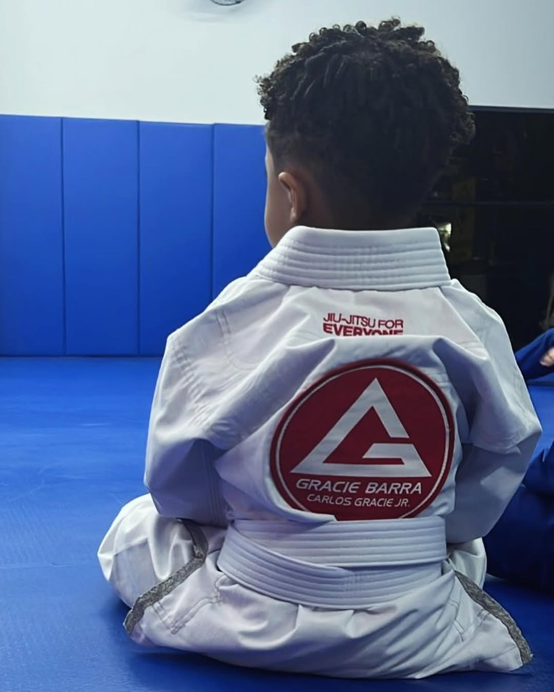 Criança de kimono branco Gracie Barra sentada no tatame
